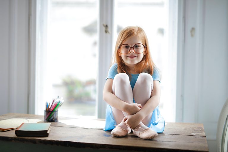 A red headed little girl wears new glasses for myopia control and is smiling
