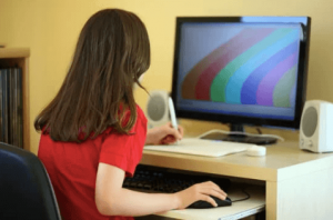 A girl uses a mouse and keyboard with a monitor at her desk