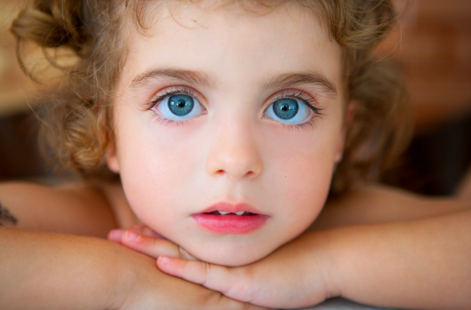 A young child with big blue eyes looks wide eyed at the camera